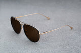 Gold aviator style sunglasses with dark brown lenses  laying flat, facing left with a quartering view.